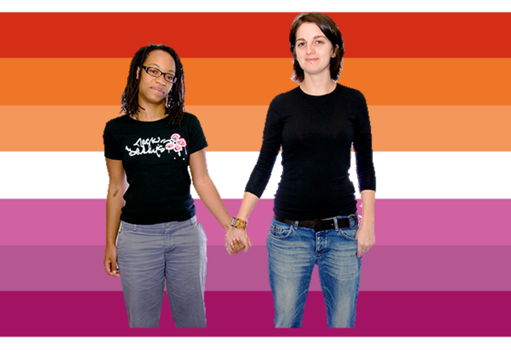 Two women holding hands in front of the lesbian flag