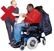 A support worker giving a man in a wheelchair a drink with a red cross over him.