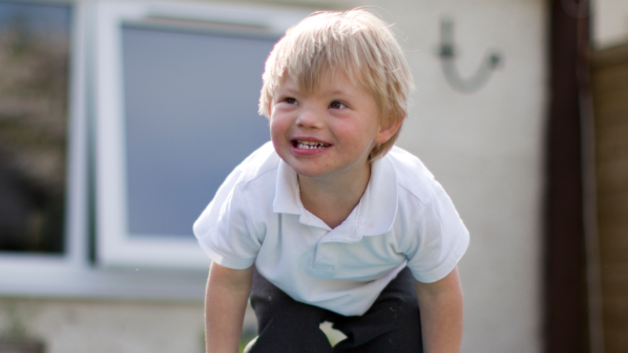 Smiling young boy with blonde hair, wearing school uniform, playing outside.