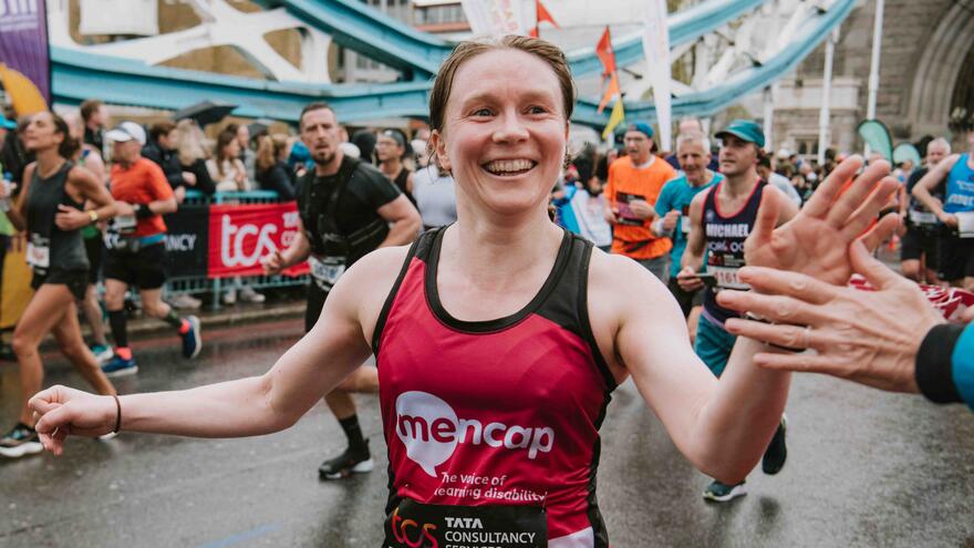A woman in a Mencap running vest running the London Marathon