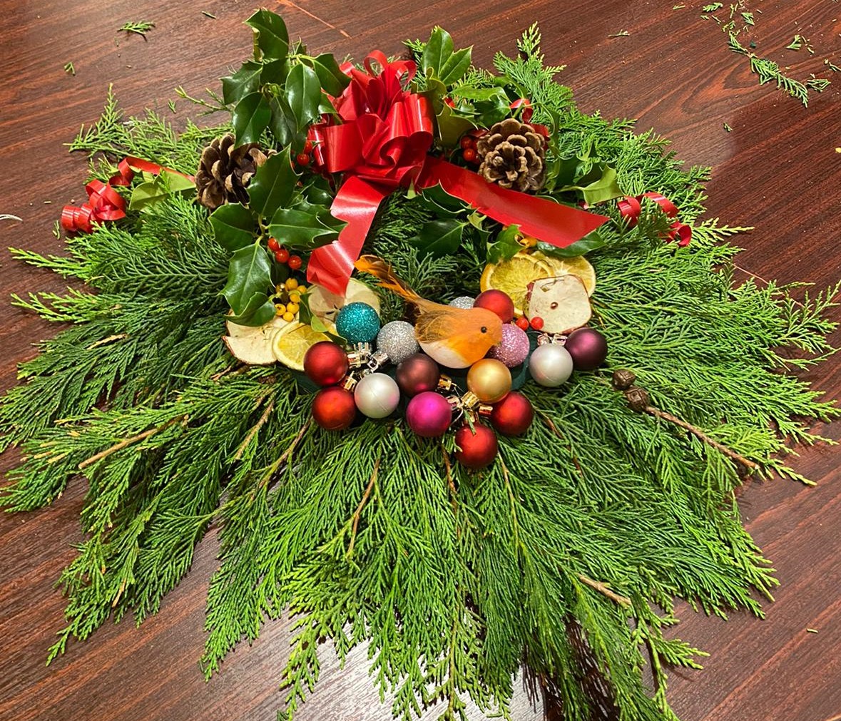 A handmade Christmas wreath with baubles and real foliage on a table top