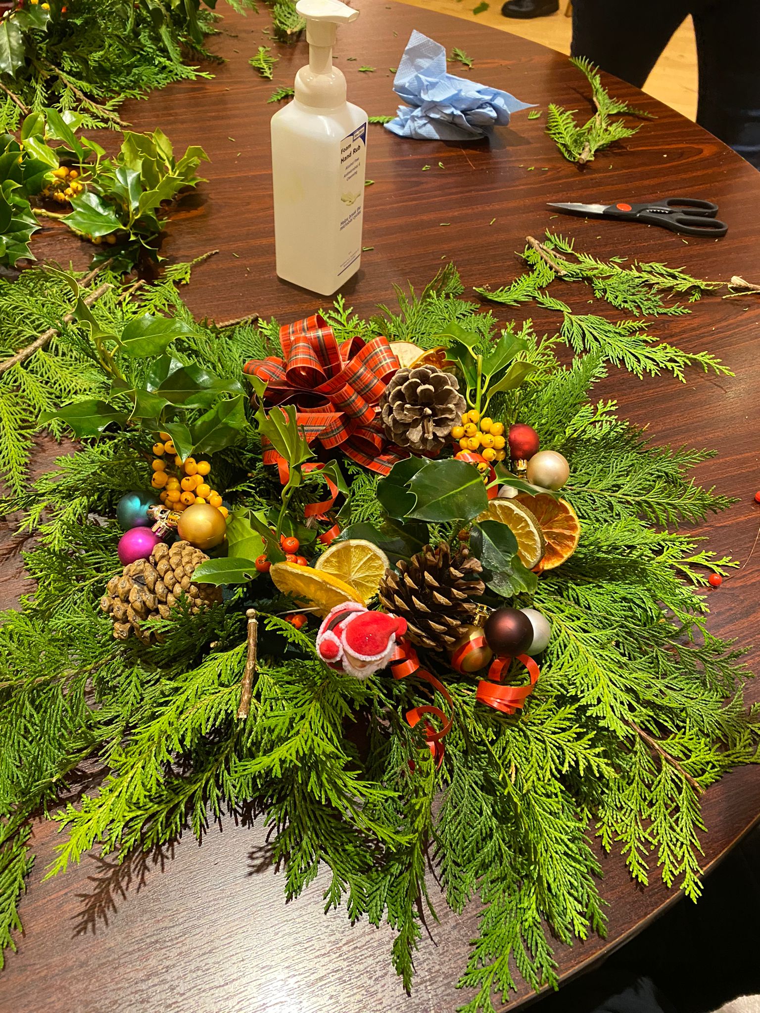 A handmade Christmas wreath with baubles and real foliage on a table top