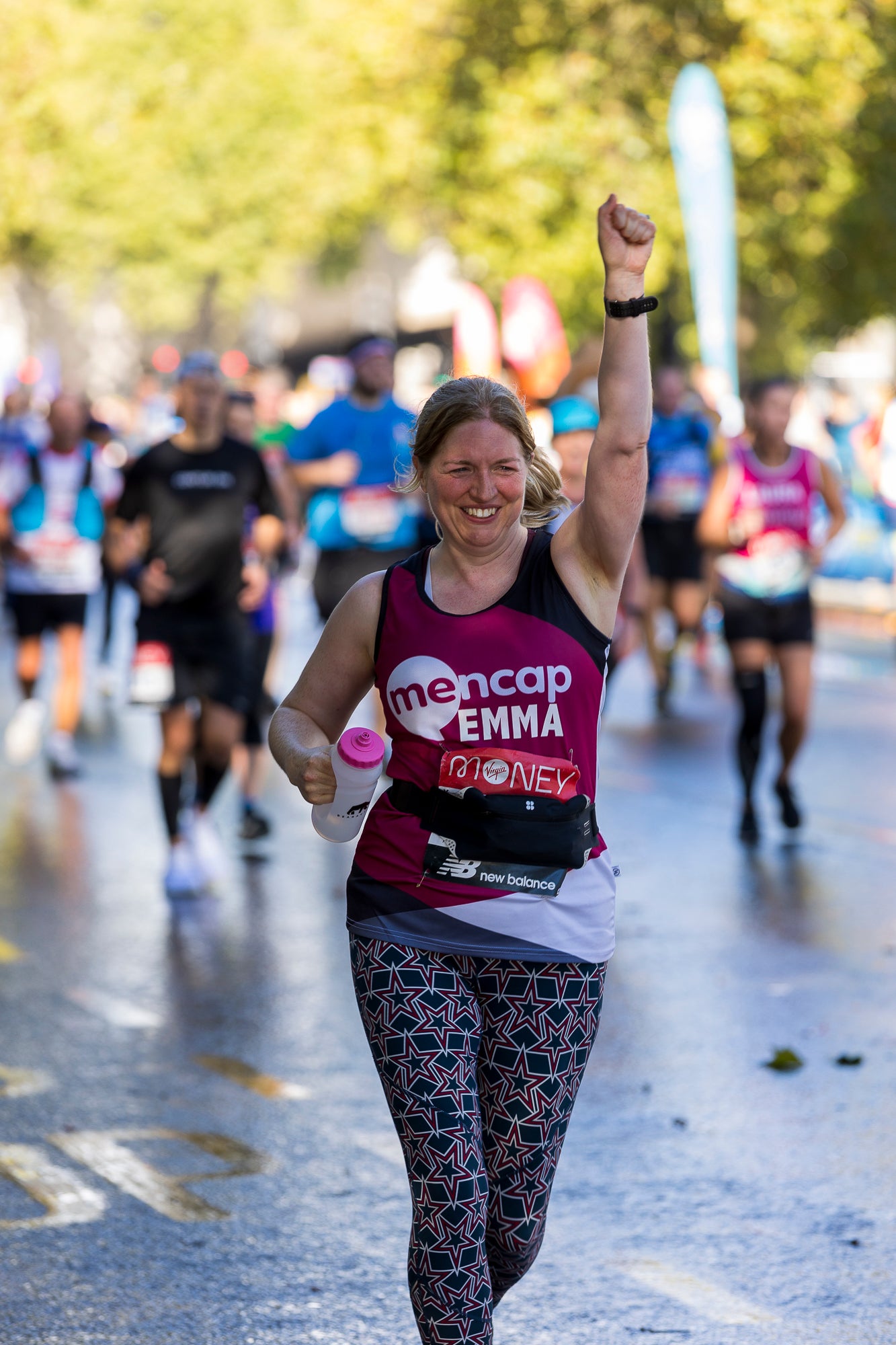 Woman running with one hand punching the air, wearing a Mencap fundraising race vest