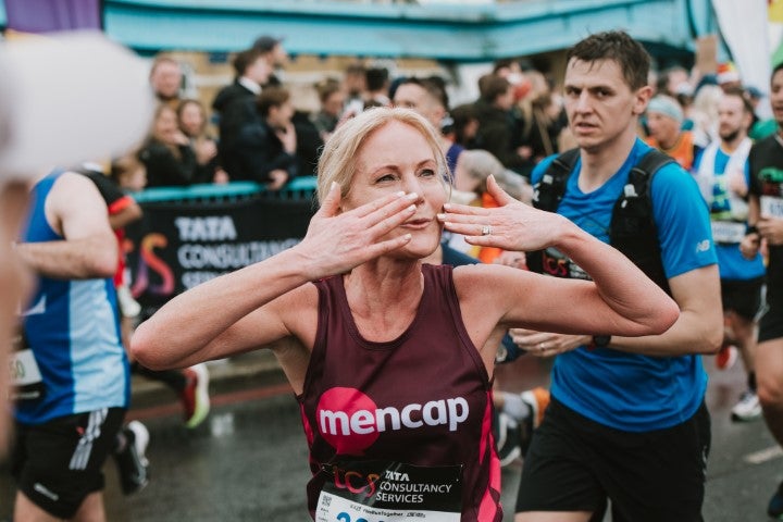 A blonde woman wearing a Mencap vest running at the London Marathon blows kisses to the crowd