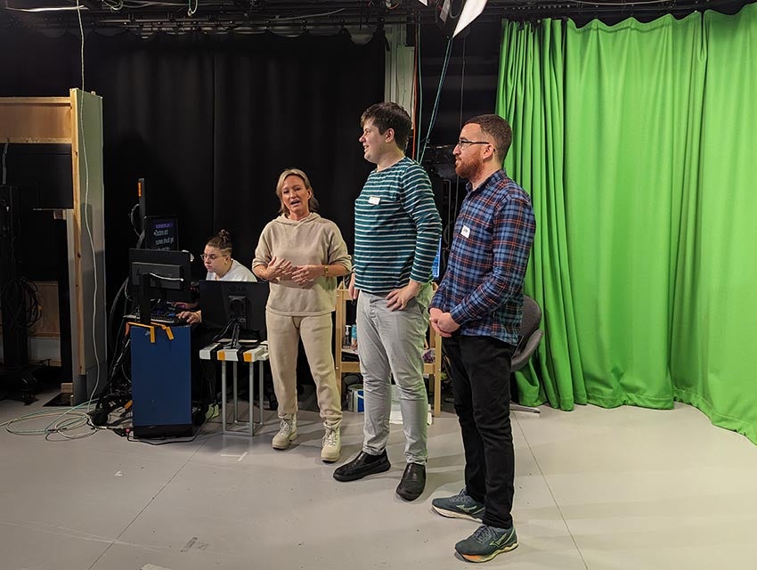 A woman and two men standing in front of a green screen in a TV studio