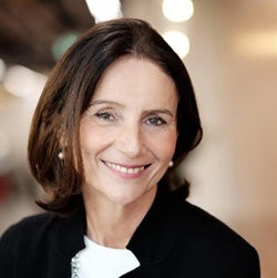 Carolyn has shoulder length dark hair and is smiling. She is wearing a black jacket over a white top