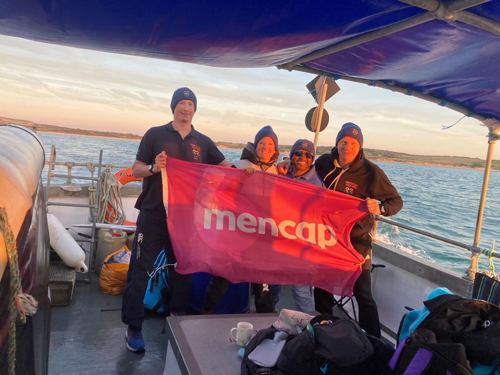 4 adults lined up on a boat holding a banner that says mencap