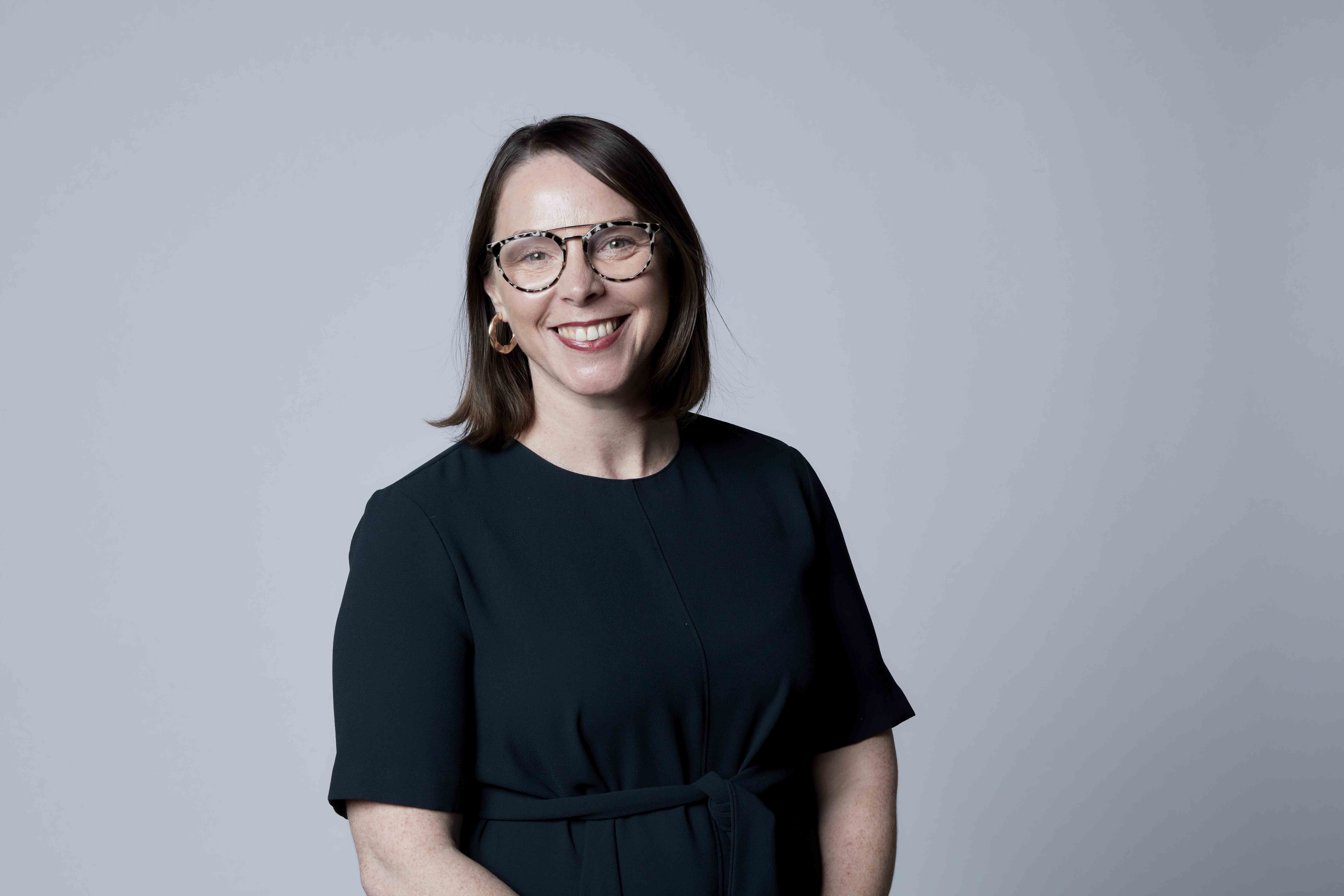 A woman from the waist up in a black tshirt smiling at the camera