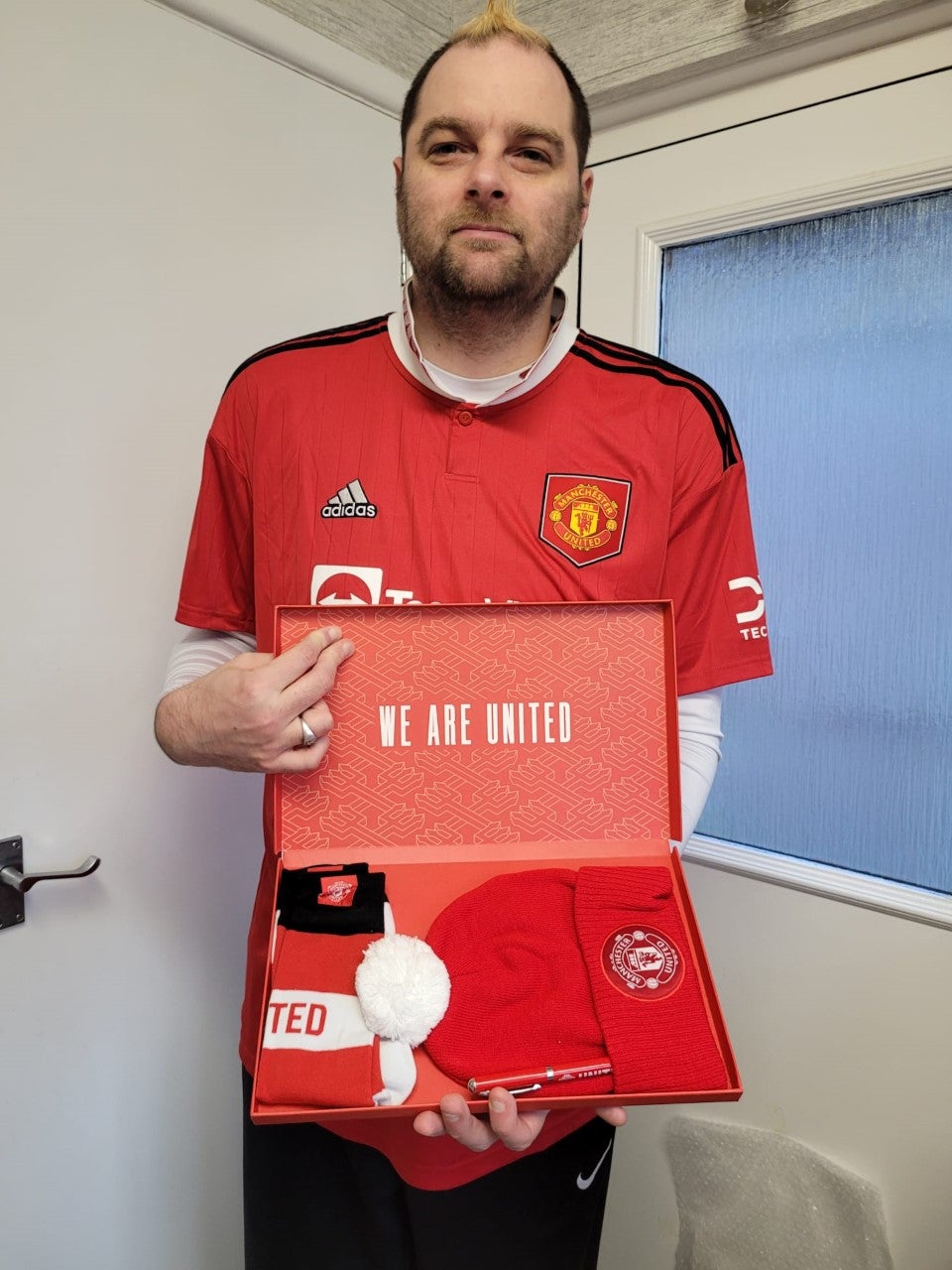A man holds a box with Manchester United scarf, pen and hat.
