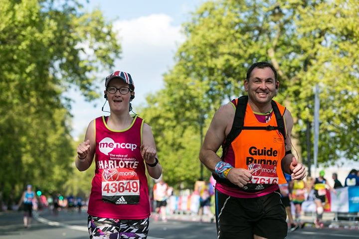 Woman wearing a Mencap running vest, running alongside a man who is her guide runner.