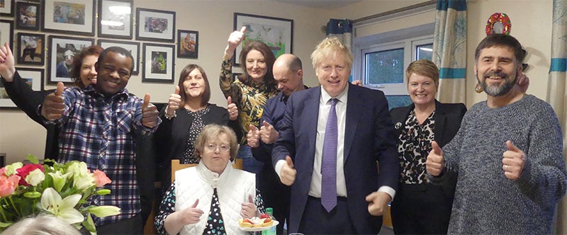 Group of people stood in Mencap service smiling and giving thumbs up sign. Prime Minister, Boris Johnson, is stood in the middle.