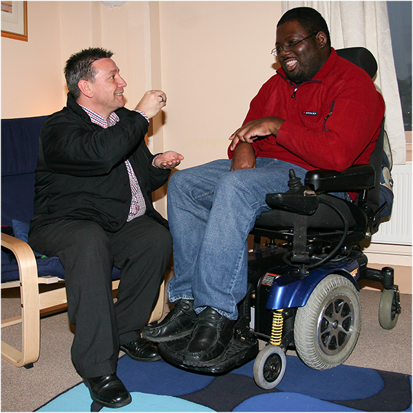 A man sitting with a man in a wheelchair in his own home