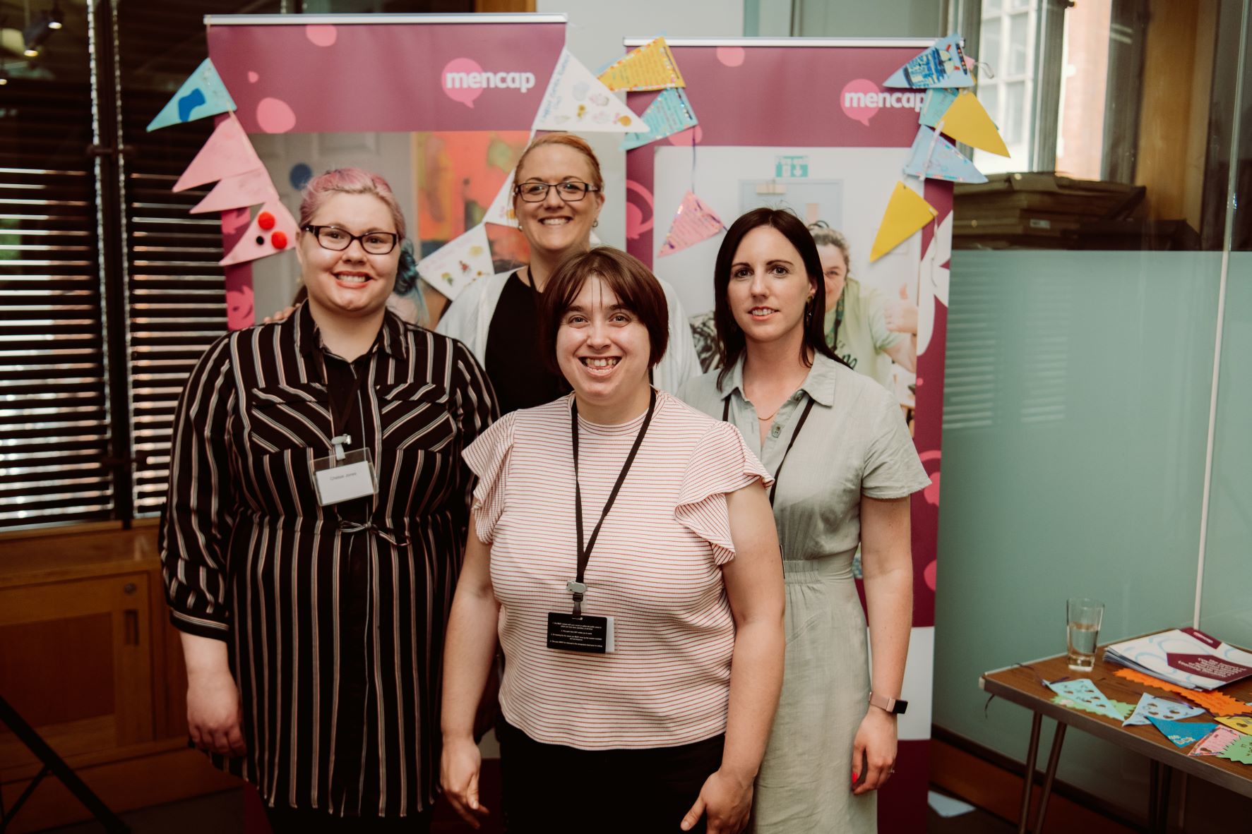 A group of people in a room standing in front of a screen of posters about Mencap