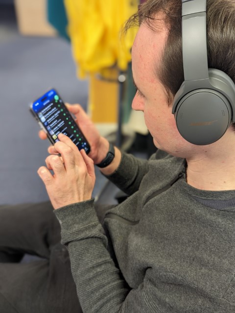 Looking over the shoulder of a man who is looking at music on his mobile phone.