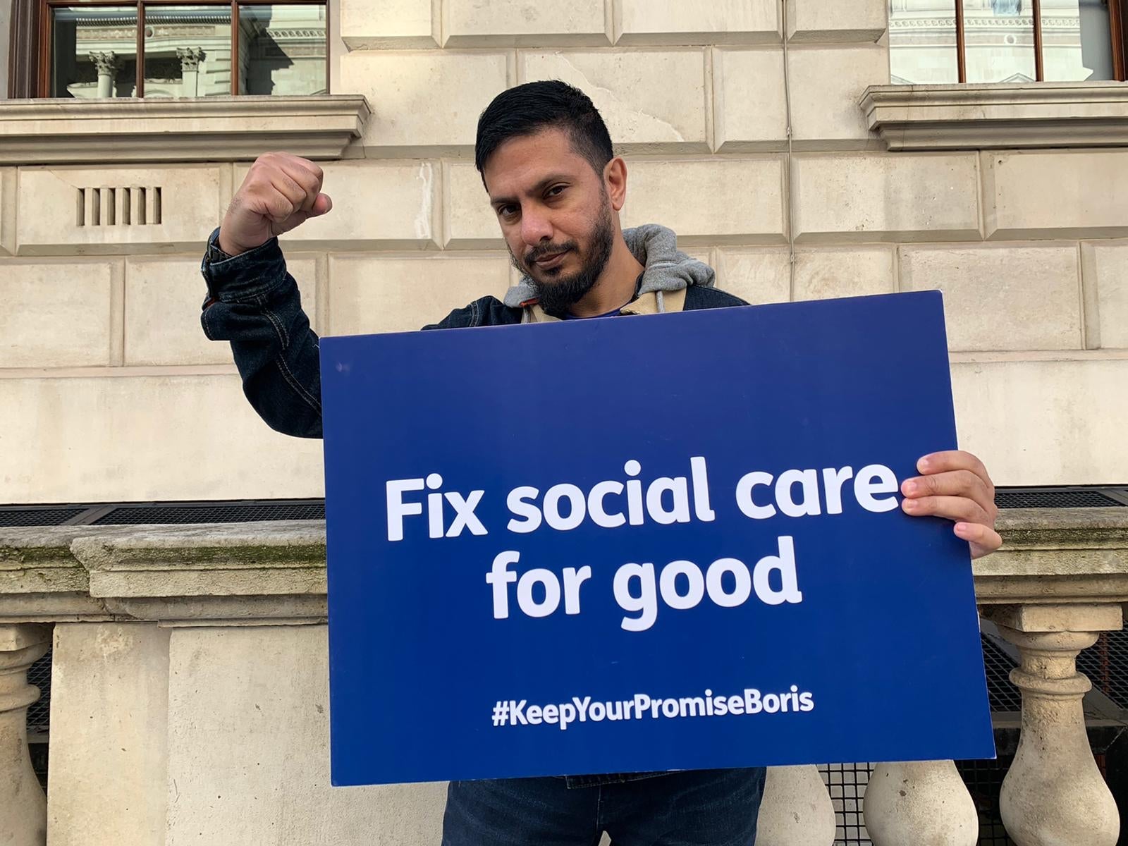 A man holds a blue sign reading "Fix Social Care for Good"