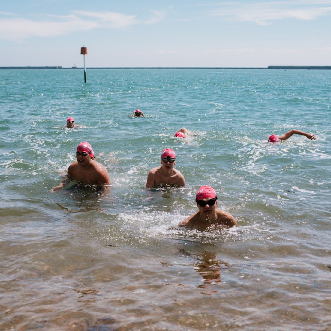 Swimmers in the sea wearing Mencap swimming caps