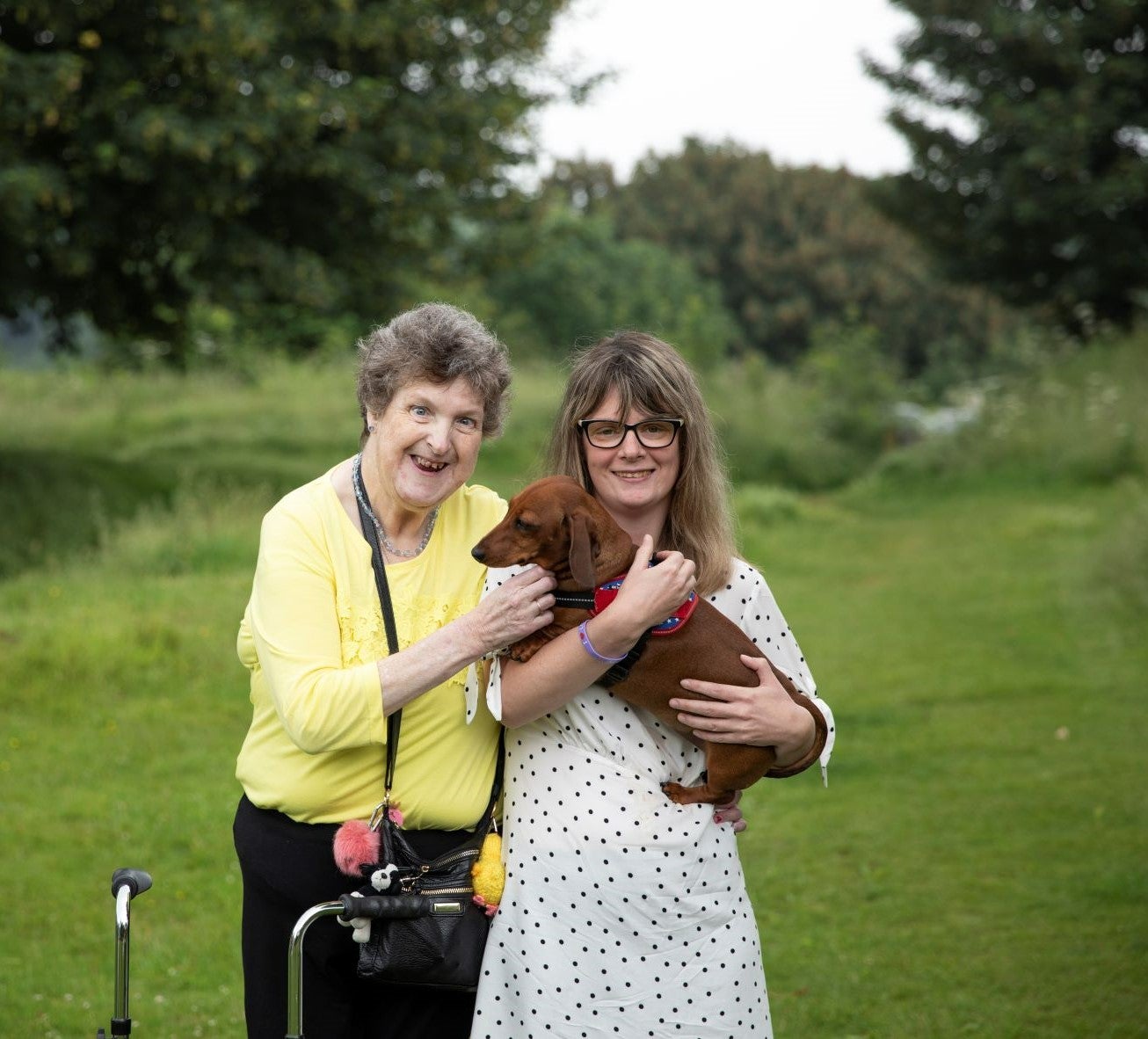 A woman with a volunteer supporter who is holding a dog in a field