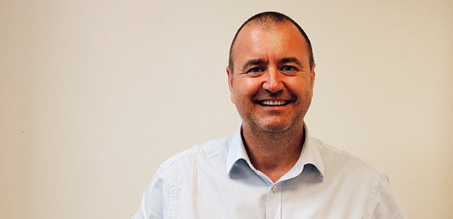 Man, Wayne Crocker, wearing a white shirt, stood smiling against a white background