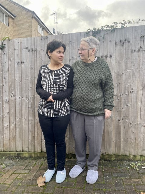 Nimali and Mary stand outside facing each other, in front of a wooden fence.