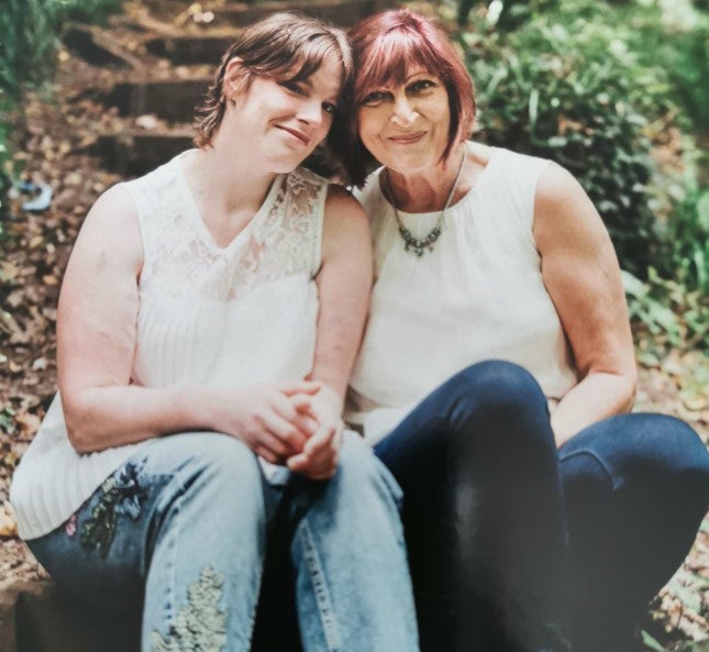 Two women sit next to each other in a wooded area
