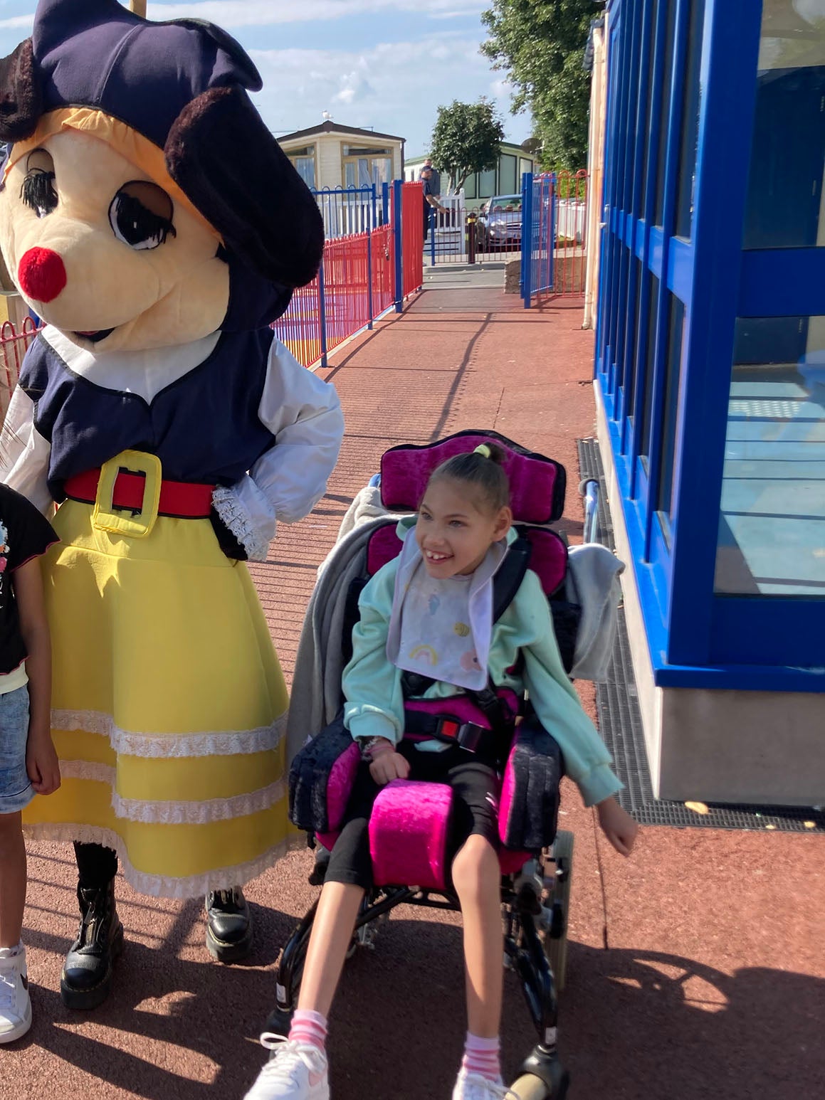 A smiling girl in a wheelchair next to a person dressed in a dog costume