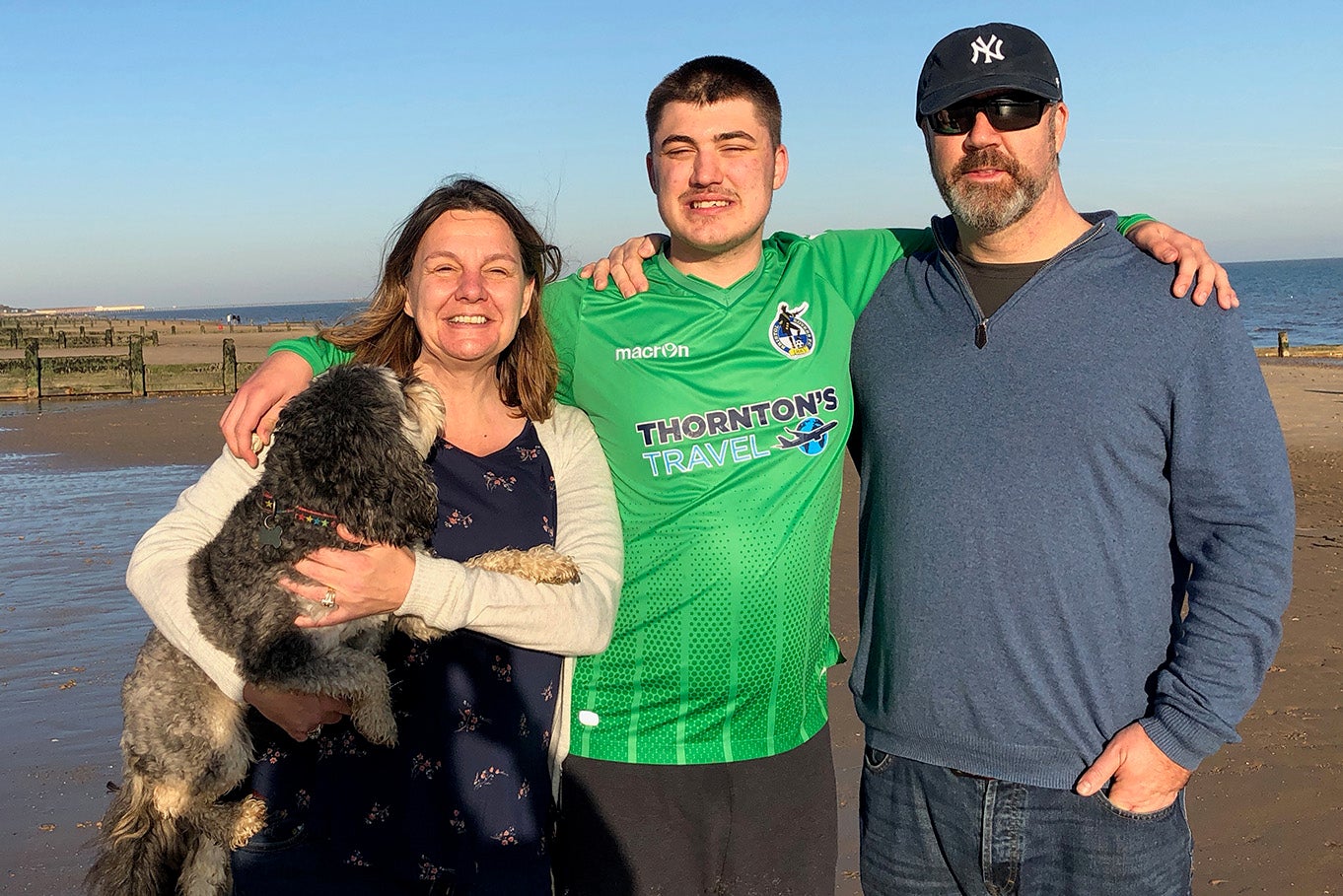 Matthew on the beach with his mum and dad standing either side of him, with the family dog