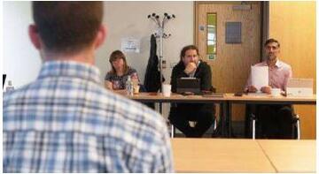 A man at a table facing three other people at a table opposite him.