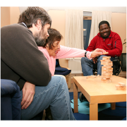 3 people sitting around a table playing a game of Jenga.