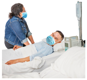 A lady sitting beside someone who is lying in a hospital bed.  They are both wearing masks.