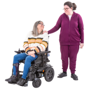 an older lady sitting in a wheelchair is looking up at a younger lady who has her hand on the back of the wheelchair.  The younger lady is looking at the older lady.  The 2 ladies look as if they are mother and daughter.