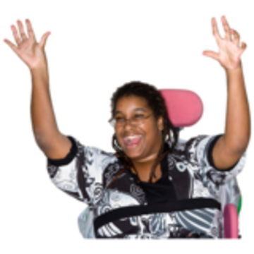 A woman with a black and white top raises her arms in the air and smiles. She is sitting in a wheelchair