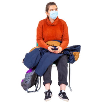 A lady wearing a facemask, sitting on a chair by herself with her phone, coat and bag beside her.