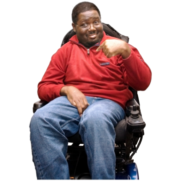 A man with a red jumper and jeans points at himself. He is sitting in a wheelchair.