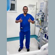 A doctor in a hospital with his thumbs up next to some medical equipment