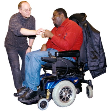 A man in a wheelchair takes a cup of tea from a male support worker.