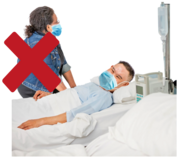 A man in a hospital bed with a visitor. The visitor has a red cross over her picture.