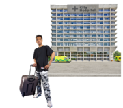 A man with a wheelie suitcase in front of a hospital building
