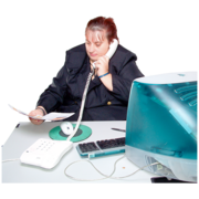 A woman sitting at a desk holding a phone to her ear, with a computer in front of her.