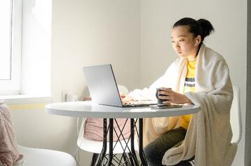 a woman sitting at a laptop with a blanket around her shoulders