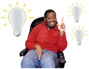 A man in a wheelchair smiling and with his hand up.  He has 3 lightbulbs around him.