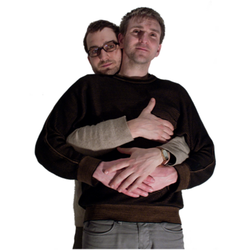 One man hugs another man from behind and holds his hand.