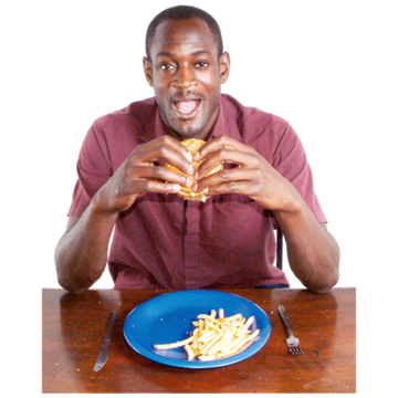 A man sitting at a table is just about to eat a burger from a plate which has chips on it