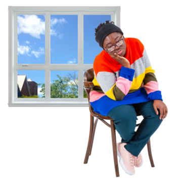 A woman sits on a chair beside a window looking sad