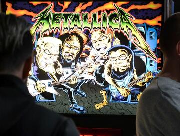 A photograph of a man looking at the screen of an arcade game with a cartoon of the heavy metal group Metallica on the screen.