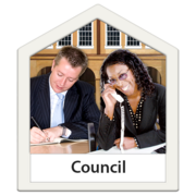 A man sits at a desk, writing. He is sat next to a woman who is smiling while on the phone. They are both in a building which is labelled 'Council'