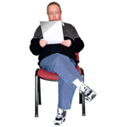 A man sat in a chair, reading from a sheet of paper.