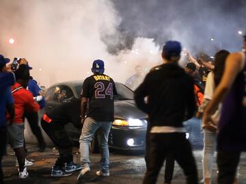 A street riot of people crowding around a car with lots of smoke