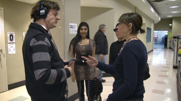 Tom is backstage wearing headphones talking to a woman whilst a backing singer looks on.