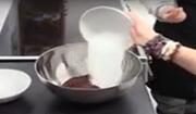 A hand holding a bowl and tipping sugar into a large bowl of melted chocolate.