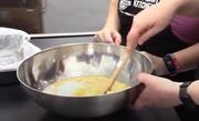 Hands holding a mixing bowl and a wooden spoon.